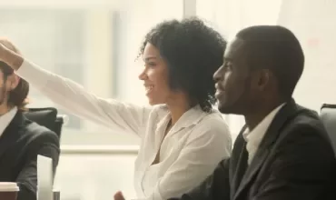 People in a meeting, one person raises a hand to ask a question.